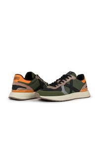 Zapatillas deportivas en verde y negro con acentos naranjas, que presentan una mezcla de materiales textiles y de ante, cordones planos y una suela acolchada.