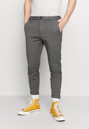Pantalons gris en mélange de coton avec une coupe slim, dotés de poches latérales, d'une fermeture à bouton et de poignets retroussés au-dessus de baskets montantes orange.