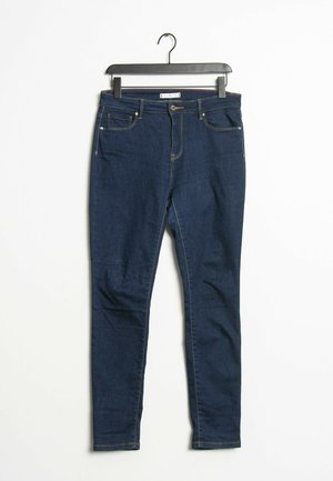 Dunkelblaue Slim-Fit-Denim-Jeans, die an einem schwarzen Bügel vor weißem Hintergrund hängen.