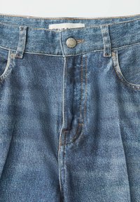 Blauwe denim jeans met tailleband, metalen knoopsluiting, lussen voor riem en zichtbare stiksels bij de voorzakken.