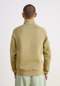 Μπεζ πουλόβερ με ψηλό γιακά, ριπ μανσέτες και στρίφωμα. Λείο υλικό με ορατές ραφές. Μόνο πίσω όψη.