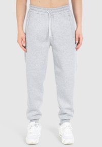 Joggers de algodón grises con cintura elástica y cordón. Tienen bolsillos laterales y piernas ajustadas, combinados con zapatillas blancas.