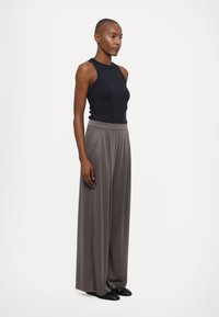 Top nero senza maniche con un design aderente, abbinato a pantaloni grigi a gamba larga a vita alta, con una texture liscia e pieghe sottili.