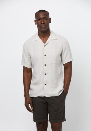 Camisa de lino gris claro de manga corta con cuello, botones negros y un bolsillo en el pecho, combinada con pantalones cortos marrón oscuro.