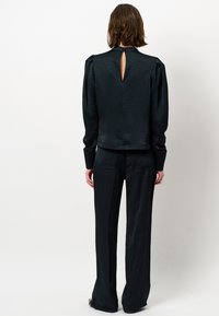 Zwarte textuur top met een keyhole achterkant, gecombineerd met bijpassende wijde broek. Beide stukken hebben een gladde, strakke stofafwerking.