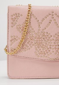 Borsa a tracolla in pelle rosa chiaro con borchie dorate che formano un motivo decorativo e una tracolla in catena dorata.