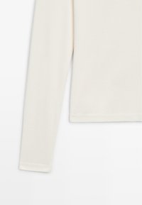 Long-sleeve cream top made from soft fabric. Features a rounded neckline and stitched hem. Simple design with no patterns or embellishments.