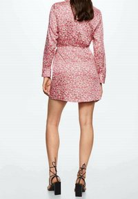 Robe fleurie rose avec manches longues, taille cintrée et ourlet court. Portée avec des sandales à talons hauts noires à brides.