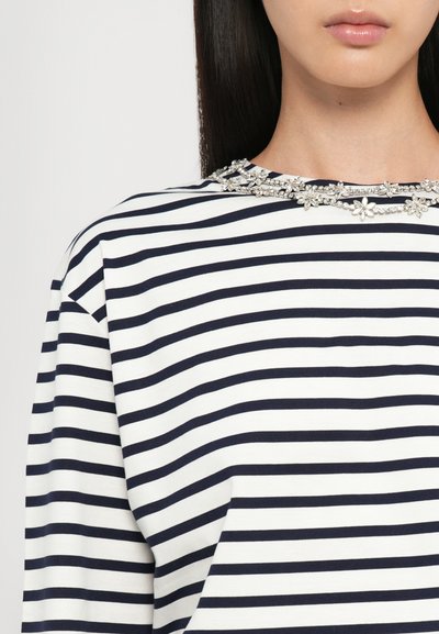 Navy and white striped top with short sleeves, featuring a jeweled floral embellishment around the neckline. Soft, textured fabric.