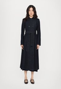 Mørk denim lang kjole med belte i midjen, dobbelspent front og kontrasterende grønn søm langs sømmene. Lange ermer og krage er inkludert.