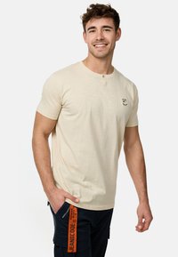 Bež majica kratkih rukava henley s okruglim izrezom i placketom sa tri gumba; sadrži mali crni logo na prsima.