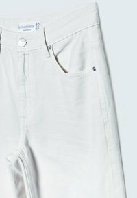 Jean en denim blanc avec une coupe droite, un design à cinq poches, des coutures visibles et une fermeture par bouton en métal. L'étiquette indique la taille 36.