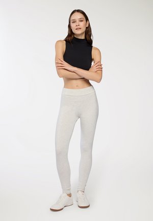Top nero senza maniche abbinato a leggins grigi chiari e sneakers bianche. I leggins presentano una vita alta e una texture liscia.