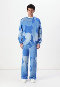 Blå sweatshirt med blommönster och matchande byxor, tillverkade av mjukt material, med avslappnad passform och ribbade ärmslut.