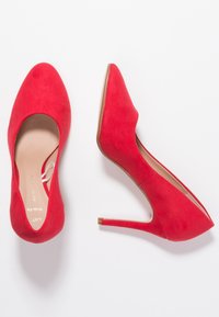 Czerwone zamszowe buty na wysokim obcasie z wąskim noskiem i smukłym obcasem typu stilettos. Wewnętrzna podszewka w jasnym beżowym kolorze.