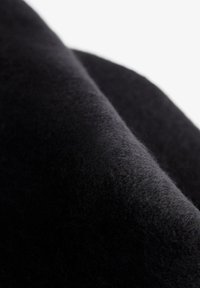 Črn volnen material z mehko, teksturirano površino, ki prikazuje fino, toplo vlaknato kvaliteto in gladko padajoč videz. Nežna variaicija globine.