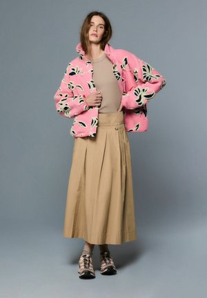 Rozā, mīksta jaka ar melniem un krēmkrāsas ziedu rakstiem, kombinēta ar bēšu krāsas krokainu svārku un daudzkrāsainām sporta kurpēm.