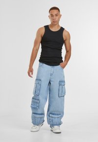 Svart ribbet tanktop og lyseblå baggy cargo-jeans med flere lommer. Hvite joggesko fullfører antrekket. Enkelt design og avslappet stil.