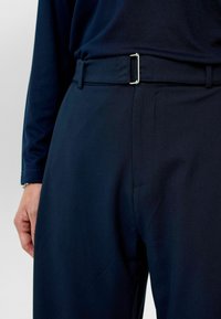Marineblauwe broek van een gestructureerde stof, met een platte voorkant en een zilveren gespriemel met een eenvoudig design. Aansluitende pasvorm met zijzakken.