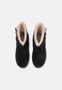 Črne semiš enolončne škornje z umetnim krznom, zaobljenim prstom in stranskimi vezmi. Imajo zanka za enostavno obuvanje.