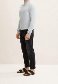 Suéter de manga larga gris claro con un cuello alto, combinado con jeans oscuros y sandalias negras de tiras; ajuste casual.