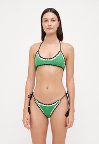 Žalias nertinis bikinis, turintis trikampį viršų ir reguliuojamas juosmens juostas, pabrėžtas juodai baltomis banguotomis kraštelėmis.
