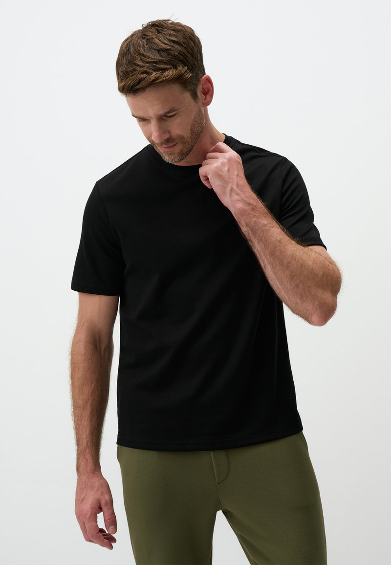 Czarna koszulka z krótkim rękawem wykonana z gładkiego, lekkiego materiału. Klasyczny okrągły dekolt, dopasowany krój, w zestawie z zielonymi spodniami.