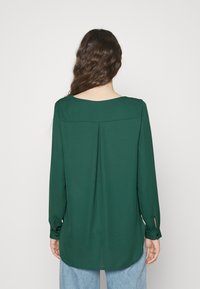 Blusa verde a maniche lunghe con scollatura tonda, dettaglio con piega sul retro e polsini con bottoni, realizzata in un tessuto morbido.