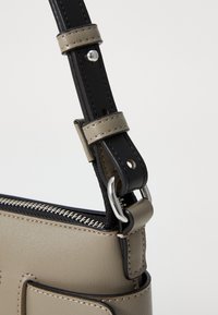 Beiger Kunstleder-Taschenriemen mit schwarzem Akzent, silberner Hardware und verstellbarer Länge mit sichtbaren Nähdetails.
