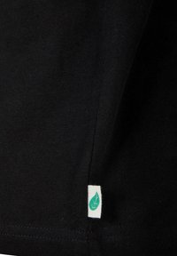 Črn bombažni T-shirt material z malo belo oznako, ki vsebuje logo zelene liste na robu. Gladka tekstura z enostavnim dizajnom.