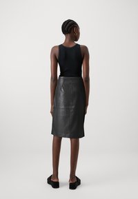 Jupe crayon en cuir noir avec un design ajusté, longueur genou et texture lisse. Assortie à un haut sans manches noir et des sandales plates.