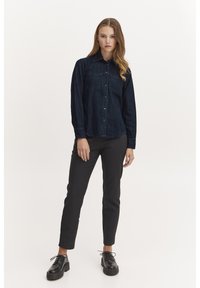 Cămașă din denim închis, cu butoni, mâneci lungi, guler și două buzunare pe piept, asortată cu pantaloni negri slim-fit și pantofi negri cu șireturi.