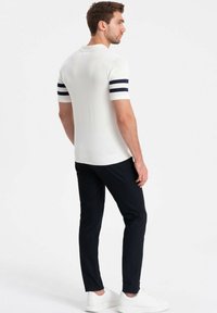 Polo shirt bianco a maniche corte con righe navy sulle maniche, abbinato a pantaloni scuri e sneakers bianche. Tessuto morbido e design aderente.