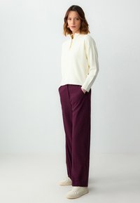 Crème ribgebreide trui met een kwart-rits kraag, gecombineerd met loszittende bordeauxrode broek, gedragen met witte sneakers.