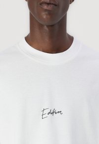 White sweatshirt featuring a soft texture, round neckline, and a black handwritten "Edition" logo on the front.