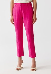 Pink tailored pants with a smooth texture, featuring a mid-rise waist, straight leg, and side slits at the hem. Pairing with nude heels.