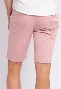 Helle rosa Shorts aus Baumwolle mit einer glatten Textur. Sie haben eine mittellange Beinform bis zur Mitte des Oberschenkels, aufgerollte Säume und ein Detail mit einer Gesäßtasche.