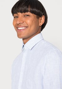 Camicia a righe blu chiaro e bianca con colletto classico. Tessuto liscio e vestibilità su misura. I bottoni sono bianchi e visibili.