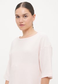 Gaiši rozā ribota īsām piedurknēm blūze ar apaļu kakla izgriezumu. Mīksta tekstūra, brīvs griezums un maigas horizontālas svītras visā audumā.