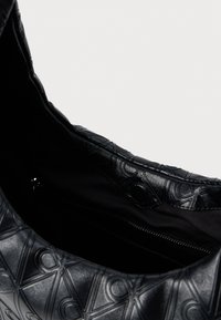 Μαύρη τσάντα χειρός με υφή δερμάτινης εξωτερικής επιφάνειας που διαθέτει γεωμετρικό μοτίβο. Το εσωτερικό είναι από μαύρο ύφασμα με τσέπη που κλείνει με φερμουάρ.