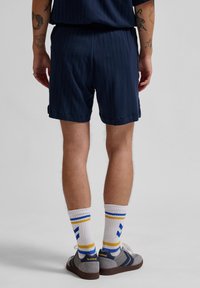 Marinblå texturerade shorts med vertikala ränder, tillsammans med vita strumpor med blåa och gula ränder, och grå sneakers.