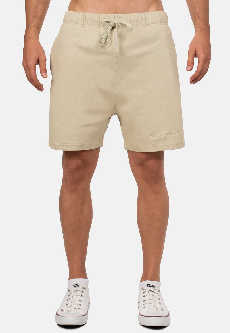 Bermuda beige con vita elasticizzata e cordoncino. Texture liscia con cuciture visibili e un sottile dettaglio del logo sull'orlo.