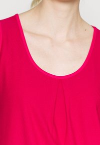 Fuchsiový top bez rukávů s kulatým výstřihem, se subtilními sklady ve středu. Hladká textura a široká ramínka pro pohodlí.