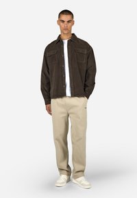 Barna kordbársony ingdzseki, két mellzsebbel, fehér póló fölött viselve. Bézs nadrág és fehér sportcipő egészíti ki az öltözéket.