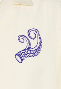 Tela color crema con un diseño de tentáculos de pulpo morado, que presenta ventosas detalladas y formas en espiral. Textura suave.