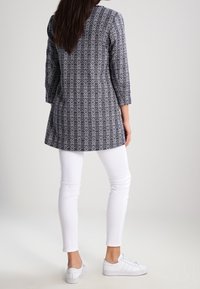 Tunique navy con motivo floreale bianco, maniche a tre quarti, orlo posteriore più lungo, abbinata a jeans skinny bianchi e sneakers bianche.