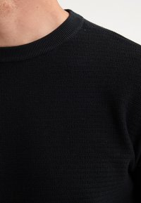 Black textured knitted sweater featuring a ribbed crew neckline and subtle horizontal pattern across the fabric.