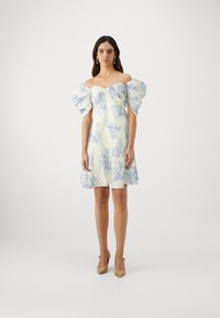 Vestido branco com padrões de corais azuis, mangas bufantes e um corpete ajustado. Combinado com sapatos de salto apontado em bege. Textura do tecido suave.