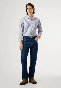 Camisola às riscas em azul claro e branco com bolso no peito, combinada com jeans de ganga azul escuro e sapatos castanhos com atacadores.