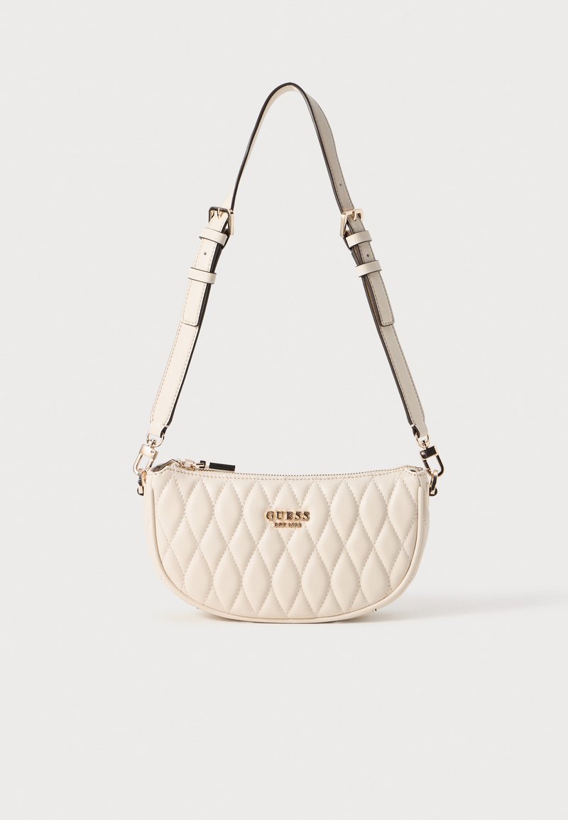 Sac à main en crème matelassé avec quincaillerie dorée et bandoulière réglable. Sa forme semi-circulaire et sa fermeture éclair arborent le logo de la marque à l'avant.